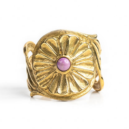 A gold-colored metal cuff bracelet with a central blue stone and decorative patterns around the edge.