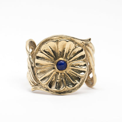 A gold-colored metal cuff bracelet with a central blue stone and decorative patterns around the edge.